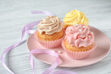 Plate with delicious cupcakes on white table