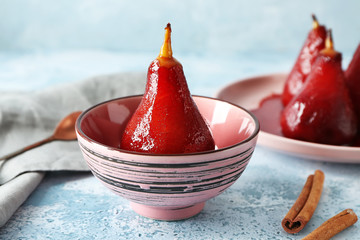 Bowl with delicious poached pear in red wine on color table