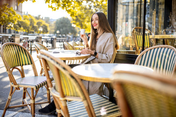 Portrait of a young woman enjoying coffee sitting outdoors at the traditional french cafe during...