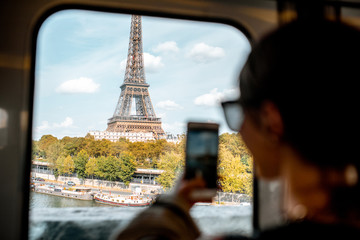 Young woman photographing with smartphone Eiffel tower from the subway train in Paris. Image focused on the tower