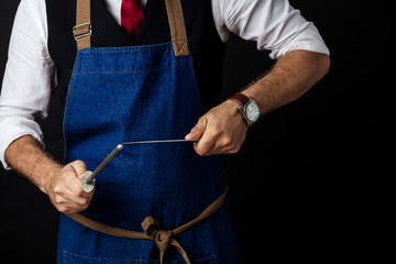 Close up mid section shot of unrecognizable chef cook in elegant uniform wearing cap and apron sharpens knife at the restaurant over black background. Small business, Service and Catering Concept