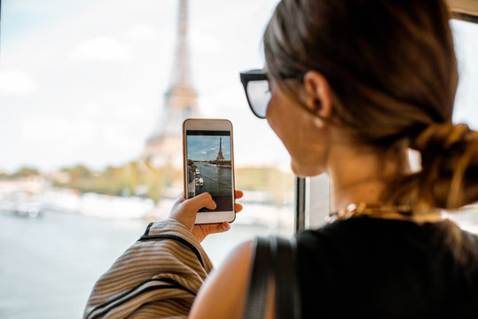 Young woman photographing with smartphone Eiffel tower from the subway train in Paris. Image focused on the phone