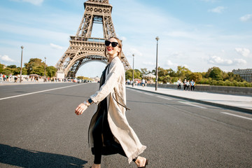 Lifestyle portrait of a young stylish woman crossing the street in front of the famous Eiffel tower during the sunny day in Paris