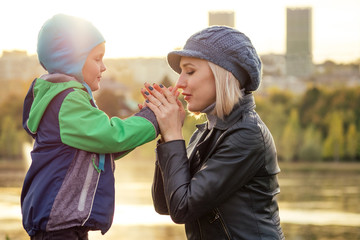 happy and beautiful blonde woman in hat kissing baby son in a warm jacket holding him in her arms in the autumn park