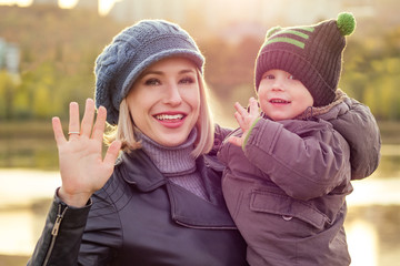 happy and beautiful blonde woman in hat kissing baby son in a warm jacket holding him in her arms in the autumn park