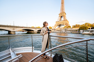 Young woman enjoying beautiful landscape view on the riverside with Eiffel tower from the boat during the sunset in Paris - obrazy, fototapety, plakaty