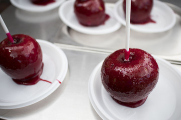 Apples covered with red caramel and sprinkles, on the wooden stick, on a plate