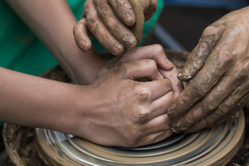 Fototapeta premium hands of a potter, helping to a boy create an earthen jar on the circle