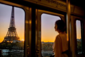 Young woman enjoying view on the Eiffel tower from the subway train during the sunrise in Paris....