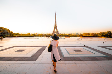 Woman dressed in coat and hat walking on the famous square with great view on the Eiffel tower early in the morning in Paris - obrazy, fototapety, plakaty