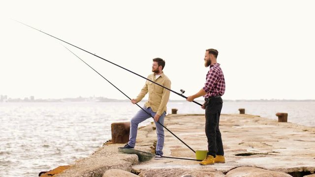 leisure and people concept - happy friends with fishing rods on pier