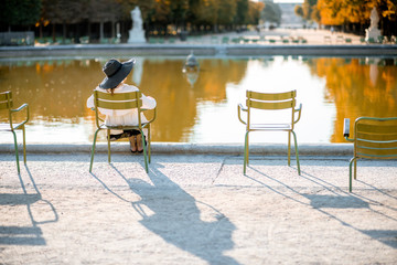Woman in hat sitting back on the famous green chair near the fountain in Tuileries park during the...
