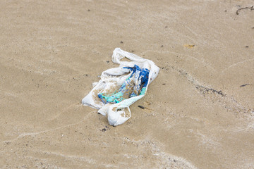 Single use plastic shopping bag washed up on a beach and part buried in the sand an example of the many pieces of garbage in the oceans around the world