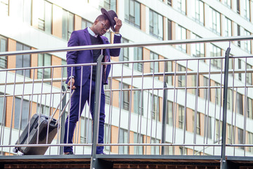 Obraz na płótnie Canvas Full body portrait of handsome traveler man African american well dressed stylish businessman walking with suitcase leaving the airport arrival home after business meeting