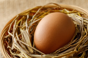 Chicken or hen egg on straw in wicker basket on sackcloth