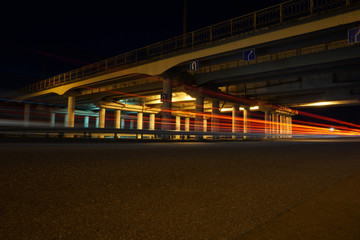 Empty asphalt road under the bridge during the night with red light trails  background. Night urban scene with car light trails in the tunnel. Long exposure.