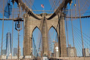 Detail of Brooklyn Bridge, New York City showing stone tower and American flag against a blue sky