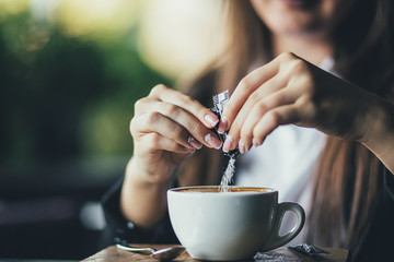Woman adding sugar to fresh aromatic coffee on table, closeup - obrazy, fototapety, plakaty
