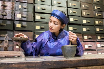 Asian pharmacist working at oriental pharmacy from the 19th century. Woman in traditional costume...