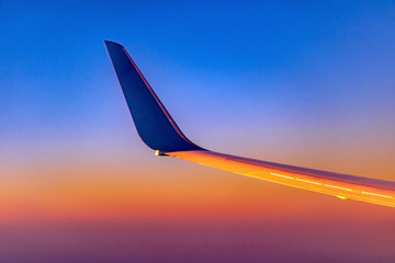 The wing with winglet of plane when a flight on background of a colorful sunset sky. Part of jet wing over orange heaven.
