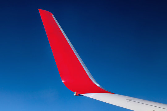 Fototapeta The red winglet on a wing of plane when a flight in a blue sky. Part of jet wing, close view.