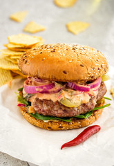 Homemade delicious juicy burger burger with red onion rings, pickled cucumbers and sauce.