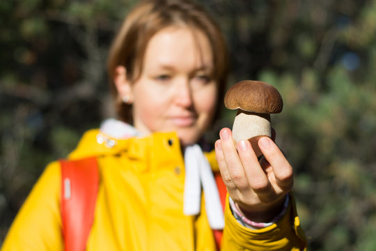 Girl in a yellow jacket with a backpack and a basket holds in her hand a porcini mushroom at the forest background