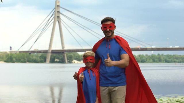 Father and son in superhero costumes showing thumbs up, motivation and teamwork