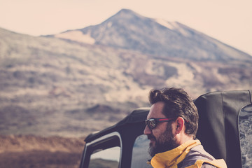 handsome middle age man with beard and sunglasses portrait. off road car and teide vulcan mountains in background for alternative vacation adventure concept