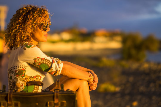 beautiful relaxed caucasian lady with white dress sitting in front of the ocean with an old luggage. travel and enjoy lifestyle concept. nice people and the nature in holiday vacation in summer time. 