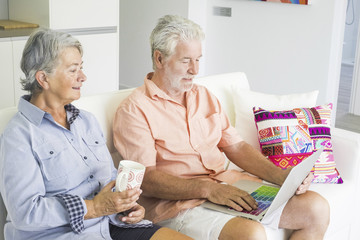 Obraz premium senior adult caucasian people couple at home using technology with internet connected laptop with coloured keyboard. together forever lifestyle for man and woman aged with white hair lifestyle