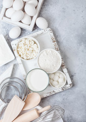 Fresh dairy products on white table background. Glass of milk, bowl of flour and cottage cheese and eggs. Box of baking utensils. whisk and spatula in vintage wooden box.Top view.