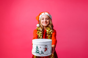 a teenage girl in Santa's Christmas hat and tinsel around her neck, gives a Christmas gift on a red background.
