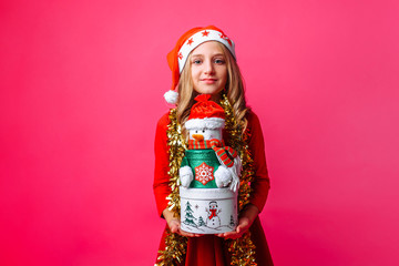 Teenage girl wearing Santa hat and tinsel on neck holding Christmas gift boxes, on red background. Christmas gifts concept