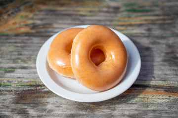 Two delicious donuts on a white dish on wooden table.