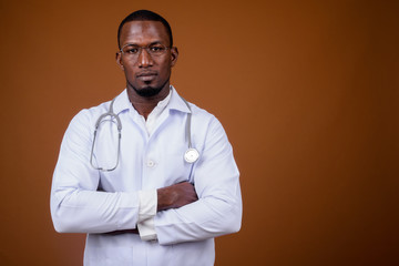 Handsome African man doctor wearing eyeglasses against brown bac