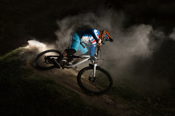 A cyclist on a mountain bike with dusty aggressive turns. Downhill riding at dark night. Bicyclist...