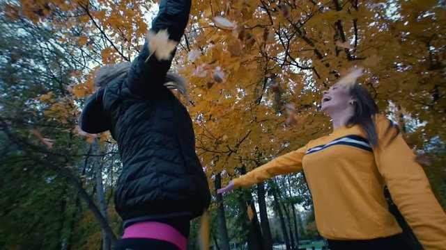 Young fit women throwing orange leaves in the air in park. Autumn
