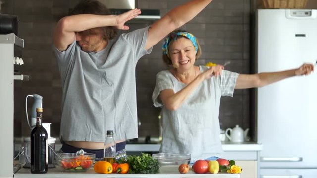 Mother and her adult son prepare food in the kitchen and have fun dancing rap. They show the double deb. A happy family
