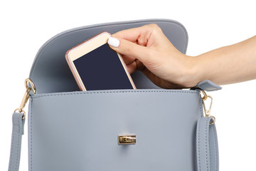 A hand put the phone in the female blue gray leather handbag on a white background isolation