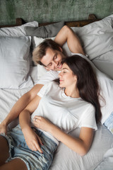 Couple in love resting at home. Young smiling girl and guy lying in casual clothes in bed at bedroom. Dating, romantic relations, amorousness or moving at new house living together concepts. Top view