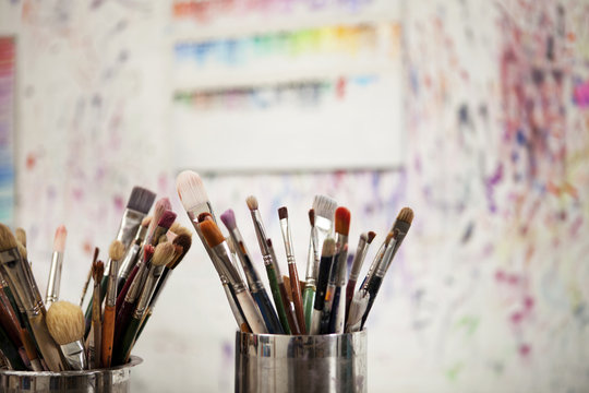Paintbrushes in containers against messy wall in studio