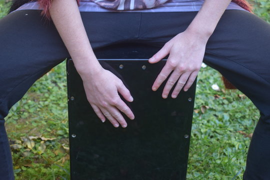 Junge Frau spielt Rhythmen auf einer schwarzen Cajon Musik Instrument auf einer Wiese