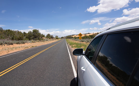 White SUV parked in front of a yellow road sign on a scenic road in Arizona