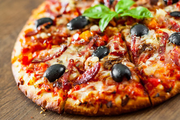 slices of Pizza with Mozzarella cheese, salami, pepper, ham, pepperoni, olives, Spices and Fresh Basil. Italian pizza on wooden background