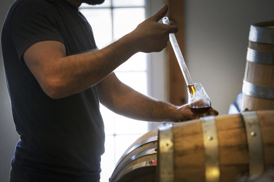 Midsection of man collecting whiskey from barrel in wineglass