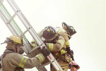 Firefighter assisting coworker in climbing ladder against sky © Cavan for Adobe
