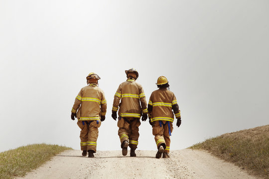 Rear view of firefighters walking on dirt road