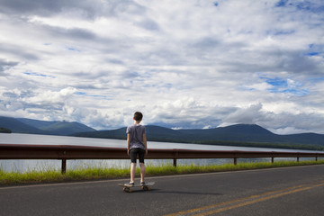 Rear view of boy standing on skateboard on road by water © Cavan for Adobe