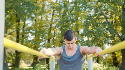 Male athlete performing difficult exercise on gymnastic parallel bars. Slim athlete a very fit guy fitness instructor or a personal trainer working out his arm muscles on outdoor beach gym as part of